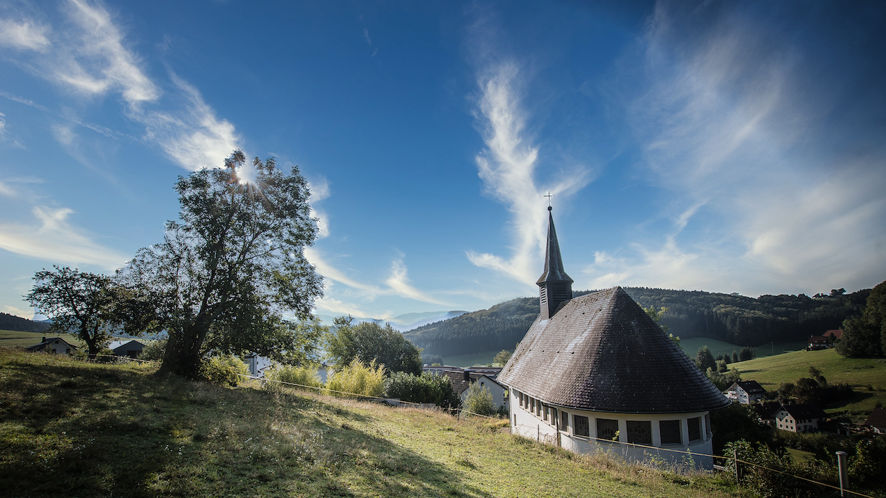 Kapelle Biederbach von hinten mit Bäumen bei blauem Himmel mit wenigen Wolken